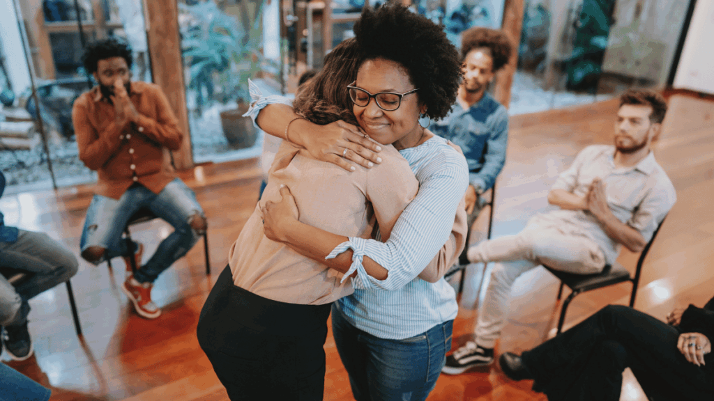 Two people sharing an emotional and supportive hug during a group therapy session, representing the empathy, compassion, and support needed when helping a loved one through substance misuse recovery
