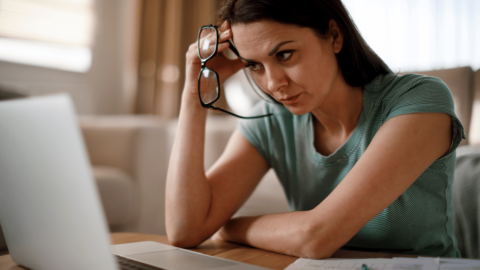 stressed out woman holding her glasses on a laptop