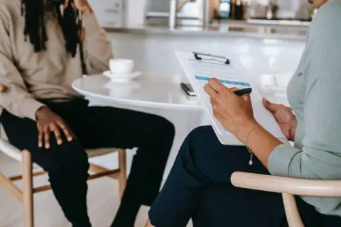 doctor with clipboard speaking to a patient drinking coffee