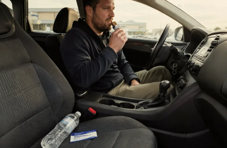 man-eating-a-snack-bar-in-a-car-with-Suboxone-medication-and water-bottle-on-the-passenger-seat