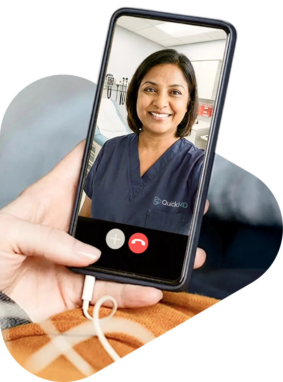 A hand holding a smartphone during a QuickMD telemedicine video call with a smiling female doctor in navy scrubs.