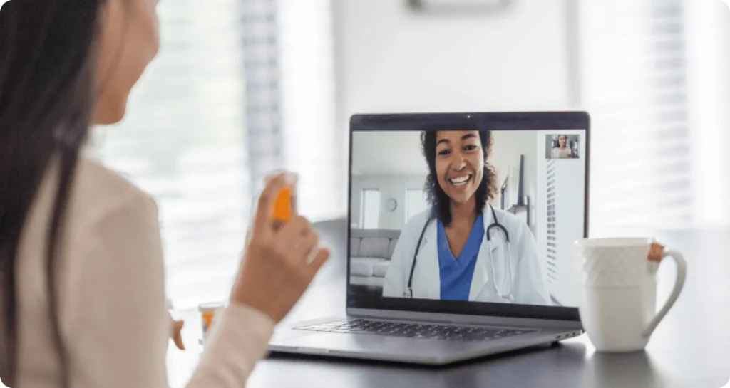 Woman holding a medication bottle during a telehealth video consultation with a smiling doctor on a laptop screen