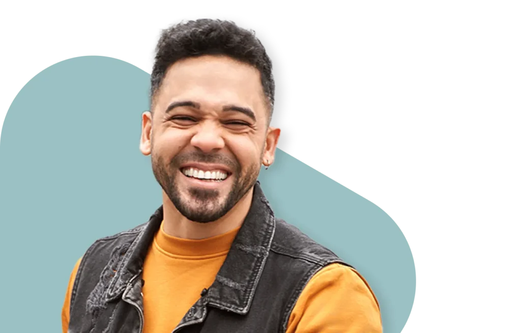 Young man with beard laughing joyfully, wearing an orange sweater and black denim vest against a teal graphic background