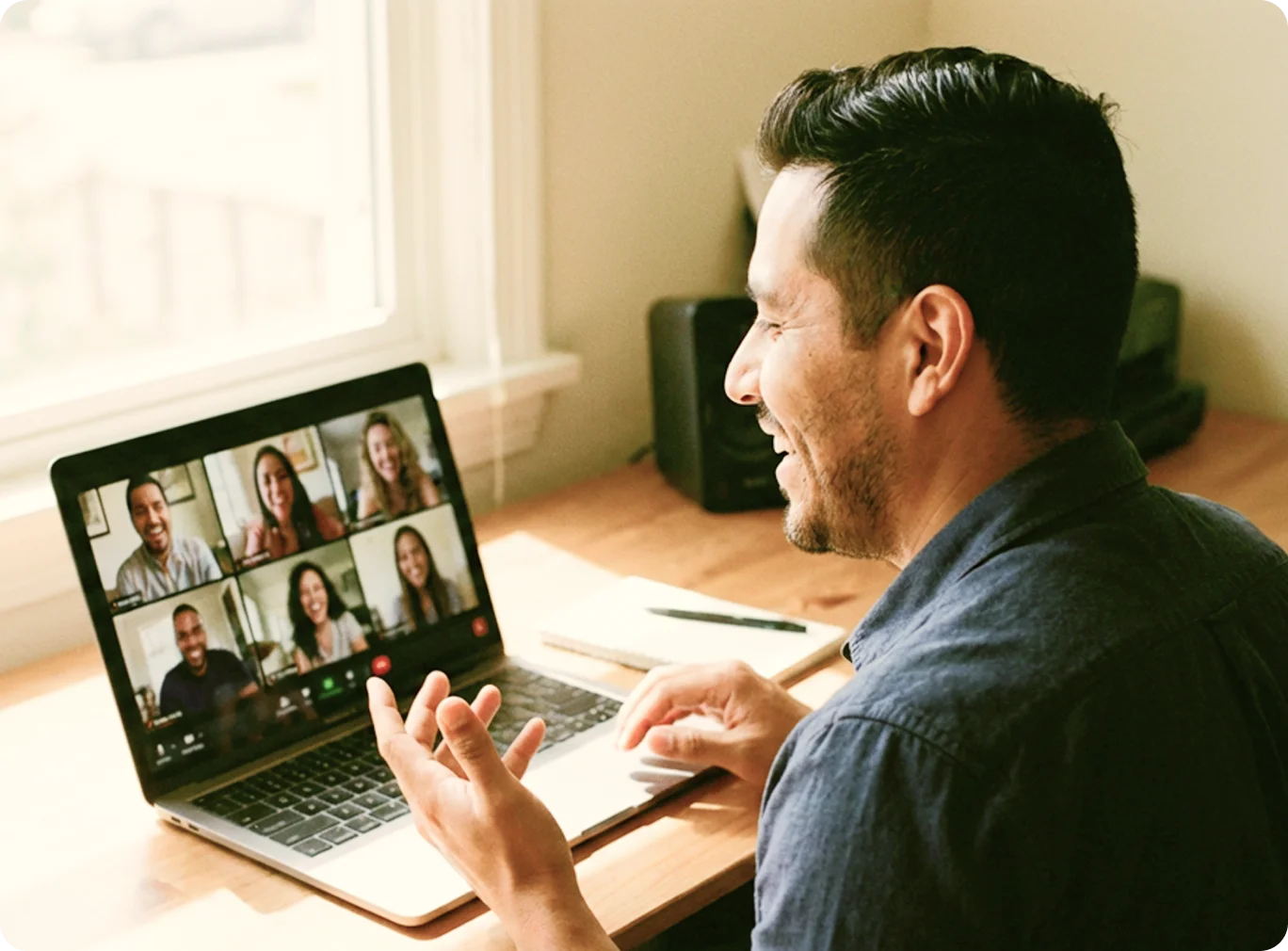 Man smiling and gesturing during an online peer support group video call with five diverse participants on a laptop