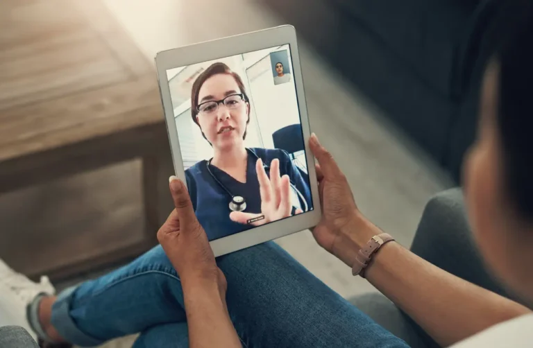 Person holding a tablet during a telehealth visit with a doctor, illustrating online urgent care for getting a doctor&rsquo;s note.
