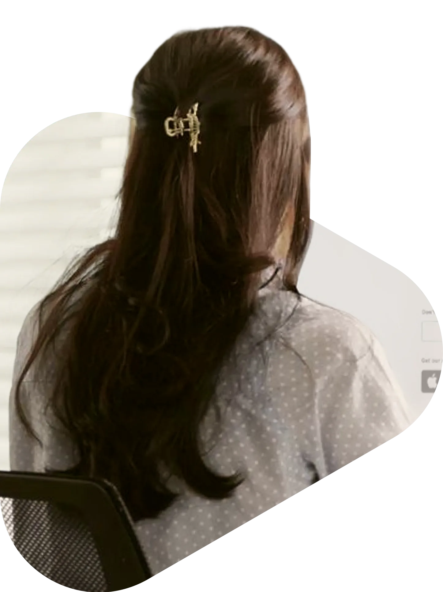 Back view of a female healthcare provider with long brown hair and a gold hair clip, sitting at a desk working
