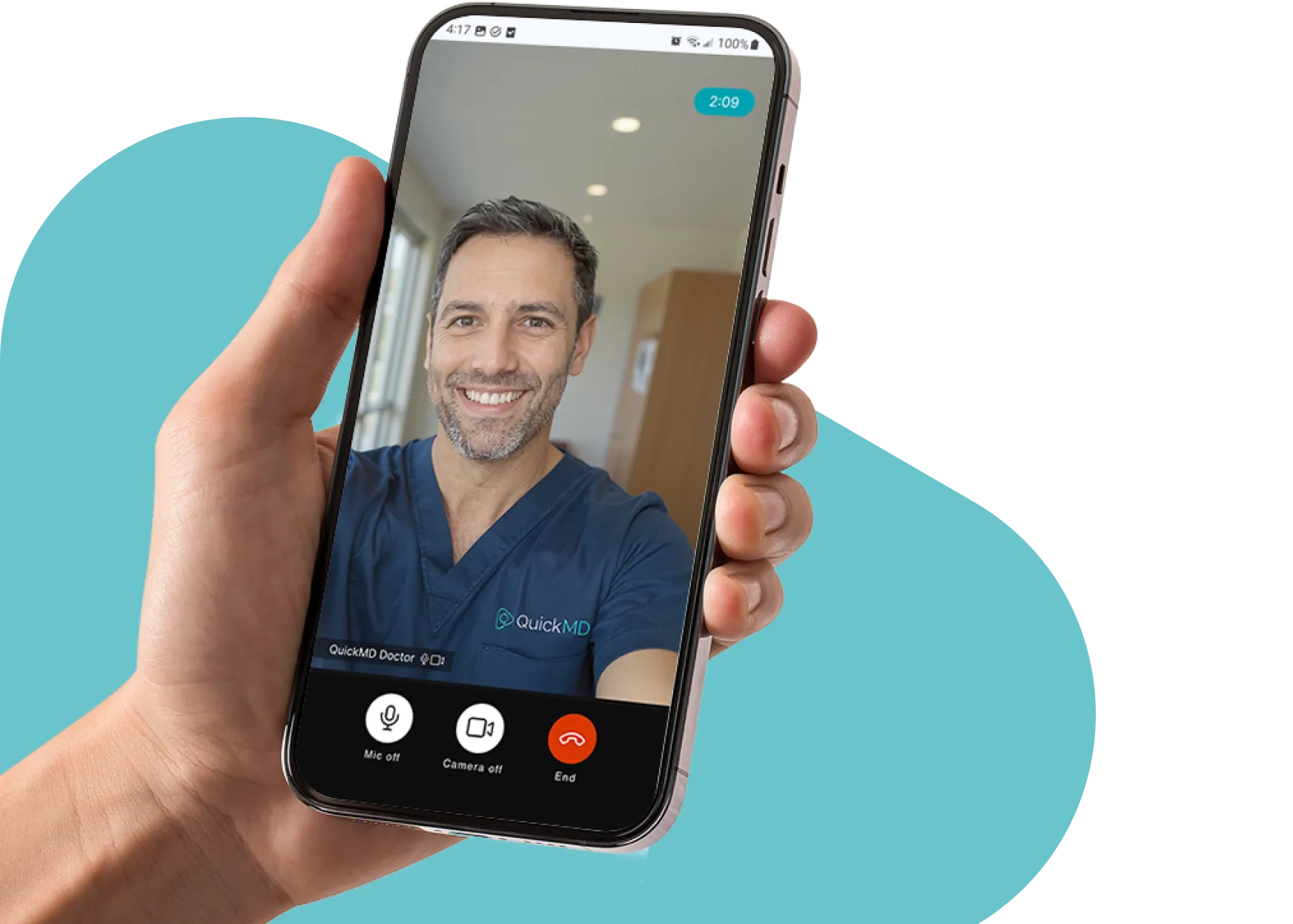 Hand holding a smartphone displaying a QuickMD telehealth video call with a smiling doctor in blue scrubs
