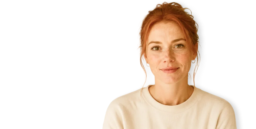 Smiling woman with red hair and freckles wearing a cream sweater against a white background