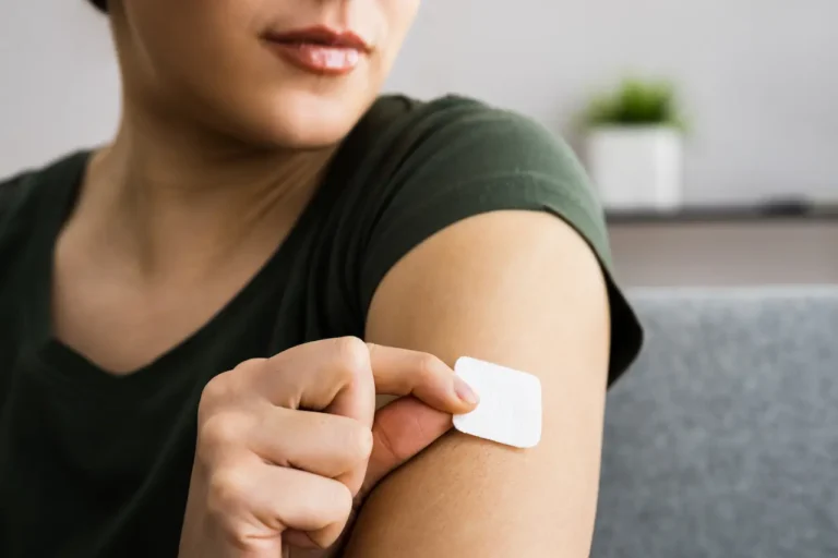 Woman applying a white estrogen transdermal patch to her upper arm for hormone replacement therapy