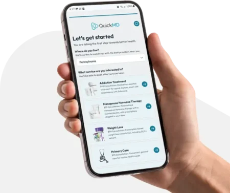 Hand holding a smartphone displaying the QuickMD app onboarding screen with healthcare service options in Pennsylvania
