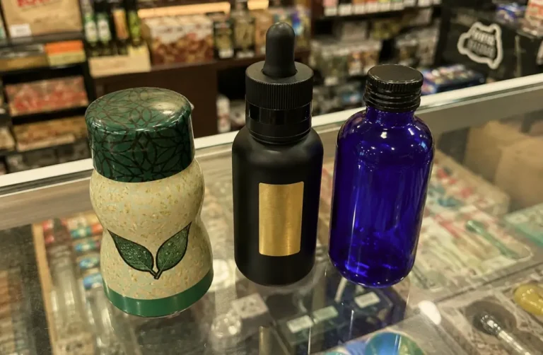 Three-kratom-products-on-a-glass-store-counter-a-decorative-leaf-motif-jar-black-dropper-bottle-and-cobalt-blue-glass-bottle