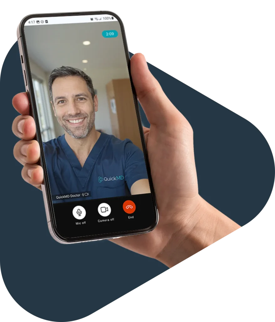 Hand holding a smartphone showing a QuickMD doctor on a telehealth video call via mobile app